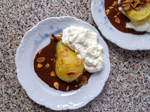 Top view of two plates with French dessert - poire belle Helene (poached caramelized pear with whipped cream, chocolate sauce and almond flakes). photo