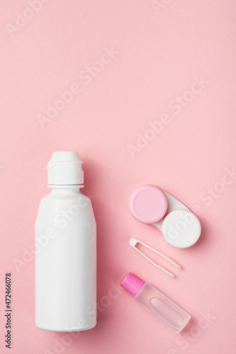 Contact lens accessories: solution, container, tweezers. Pink background, copy space.