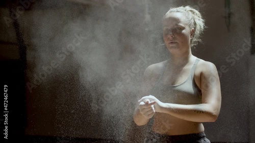 Medium shot of athlete clapping hands with magnesia powder. Chalk powder exploding into dust particles in sunlight. Powerful woman getting ready for boxing training. Sport, kickboxing concept photo