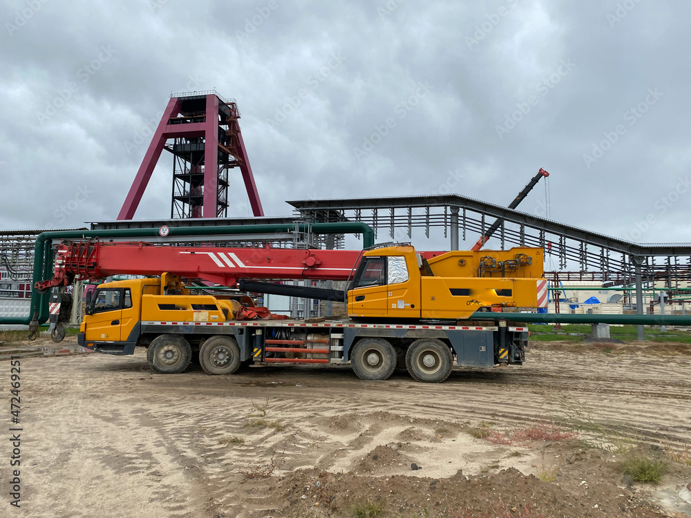 A large blue truck crane stands ready to operate on hydraulic supports on a platform next to a large modern building. The largest truck crane for solving complex tasks