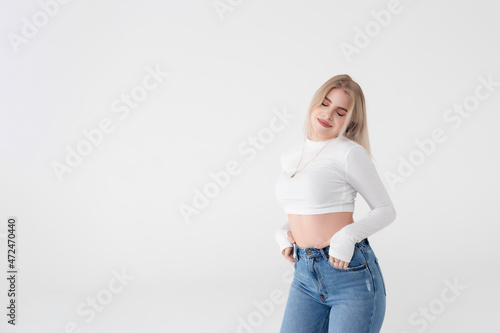 Happy and beautiful young woman in a white sweater enjoys standing on a white background