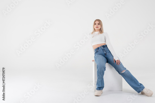 A young girl in a white sweater and jeans sits and poses on an isolated white background in the studio. People lifestyle concept. Copy space for copy