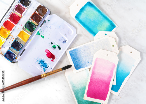 Open watercolor paint box with brush painting gift tags.
