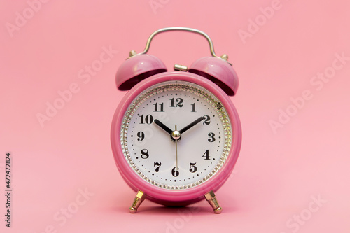 Little pink retro alarm clock on pink isolated background. It's time to wake up and go to school or university, do homework. Time to relax after a long day's work.