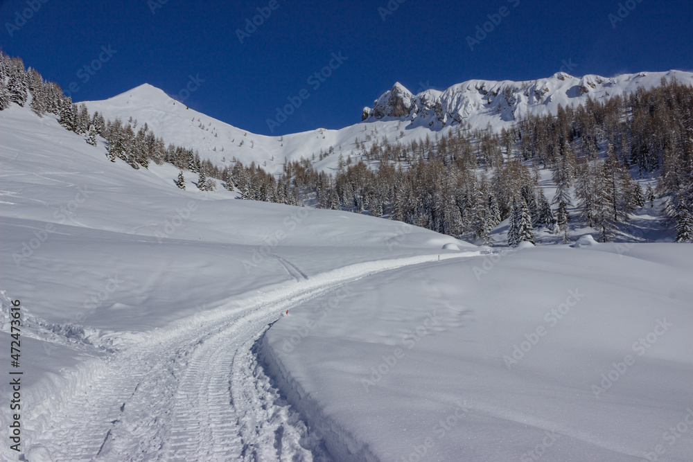 Italian mountain winter landscape. Expanse of snow and a trace left by a snow cat with the background of mountains and the blue sky. Staulanza Pass, Italy.