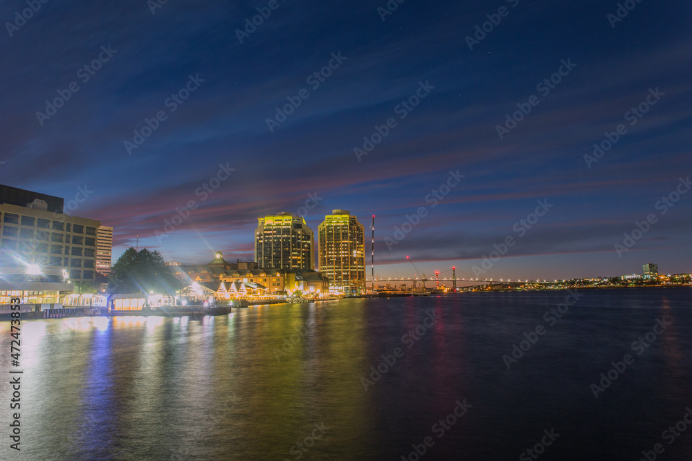 A dynamic night view of bustling Halifax Waterfront Harbor front with prominent business and financial buildings and restaurants with the MacDonald Bridge at background, Nova Scotia, Canada. 