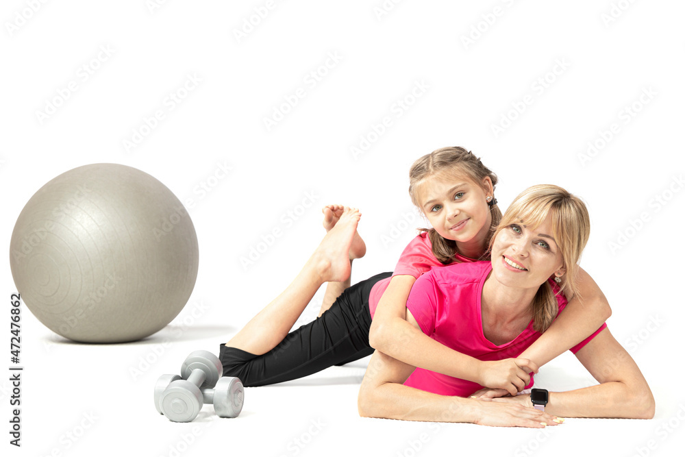 Pretty young woman and her daughter lie on a yoga mat in a fitness studio looking at the camera and smiling isolated on a white background. Pretty young woman and her daughter lie on a yoga mat in a fitness studio looking at the camera and smiling isolated on a white background.