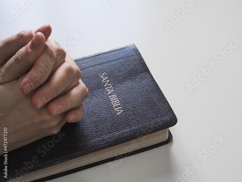 Hands linked on holy bible with copy space on white background. The book says in Spanish: Holy Bible
