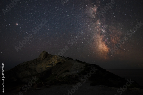 A large panorama of a beautiful view of the sea among the mountains and a beautiful starry sky with the Milky Way. The city by the sea glows at night in the distance © dmitriydanilov62