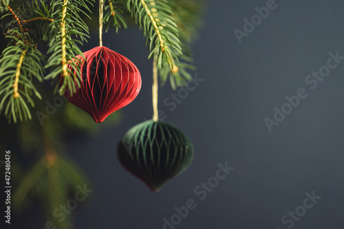 Red and green Christmas paper decorations on fir branches against dark turquoise background.