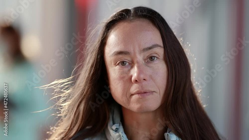 Close-up of an adult woman looking into the camera. Portrait of a serious girl standing in the rays of the setting sun.The concept of people and emotions.