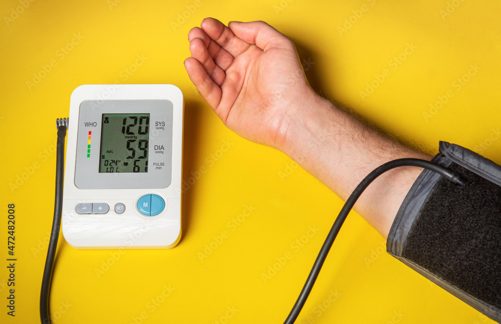 Person measures their own blood pressure at the yellow medical table. Taking care of your own health. Digital blood pressure machine shows a good result Person measures their own blood pressure at the yellow medical table. Taking care of your own health. Digital blood pressure machine shows a good result