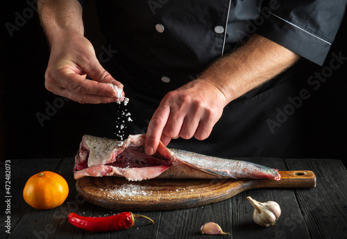 Cook prepares fresh fish sprinkling salt. Preparing to cook fish food. Working environment in the restaurant kitchen. photo