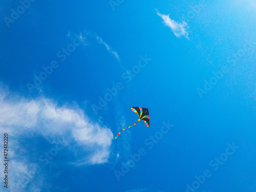 Kite blue sky. Colorful high flying toy. Air kite fly on wind clouds. Rainbow kite in summer background. Concept of dreams, freedom, childhood.