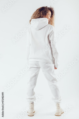 Woman with thick curly hair in a white suit from a hoodie and sweatpants back view. photo