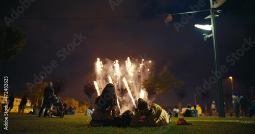 View of people gathered in park enjoy and watch incredible fireworks show, family lay on picnic blanket and look at sky on fireworks lighting up. Concept celebration or festivity on summer day