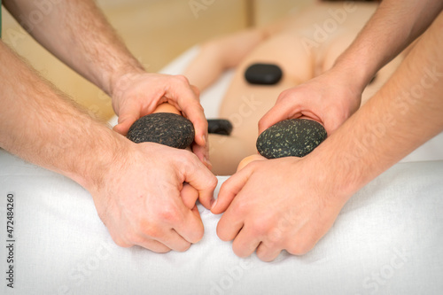 Two masseurs make a foot massage with a hot stone in four hands at the spa photo