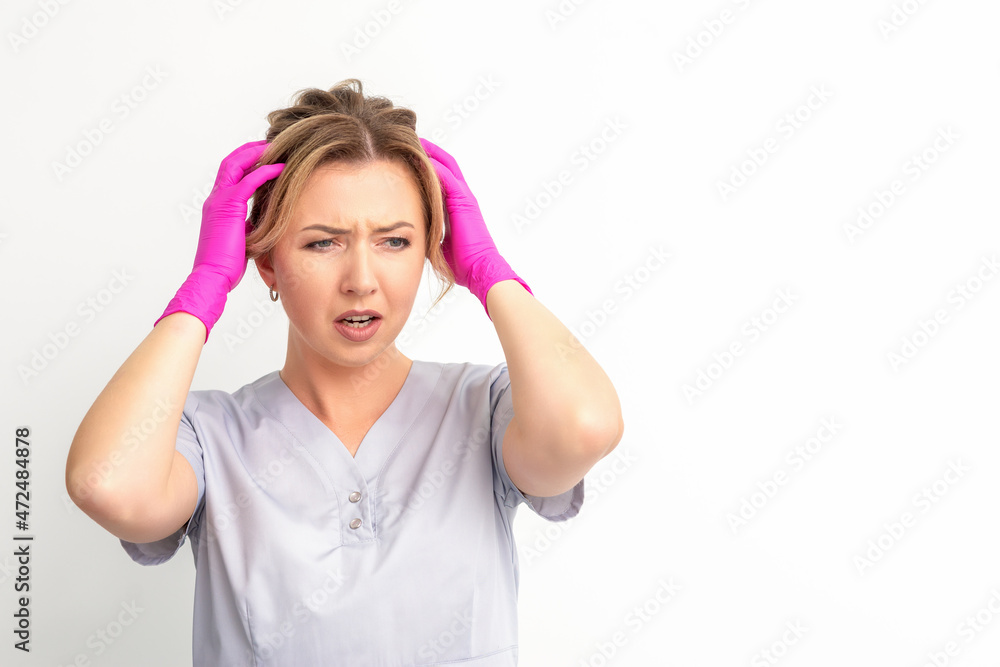 The emotionally shocked young female medical worker holding hands on her head fell into panic on white background, infection, epidemic, virus, and disease concept The emotionally shocked young female medical worker holding hands on her head fell into panic on white background, infection, epidemic, virus, and disease concept