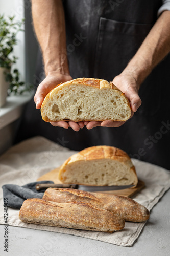 an adult European male baker holds a round fresh bread in his hands. a man in a bakery holds a yeast-free bread on sourdough and a baguette. cool and healthy bread for the whole family. vegan food for