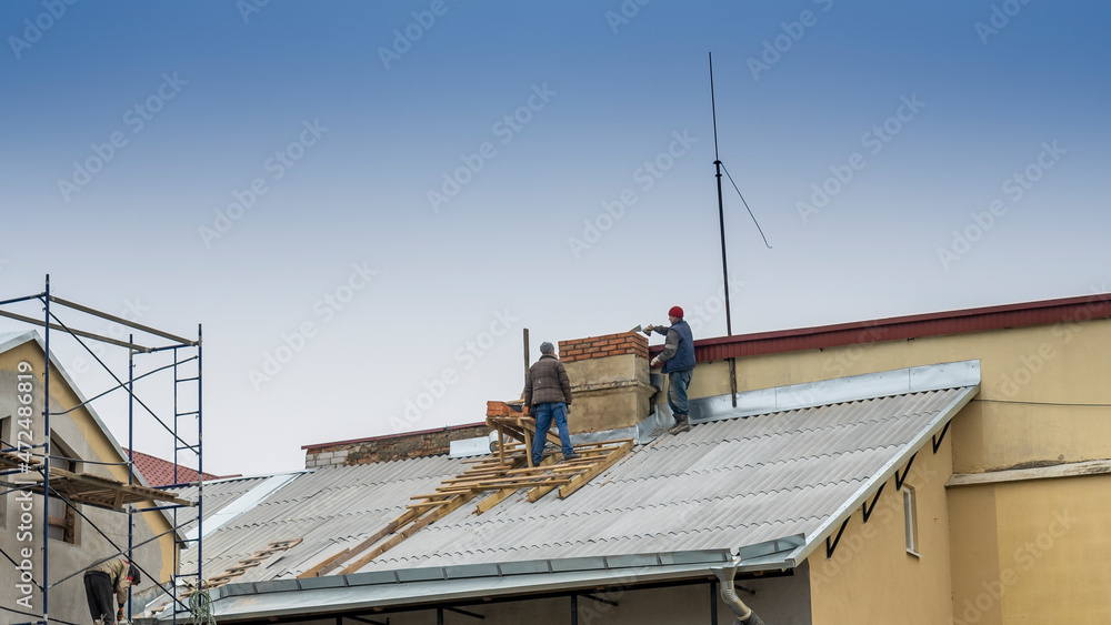Construction workers put shingles on a roof. Workman install new roof on old building.
