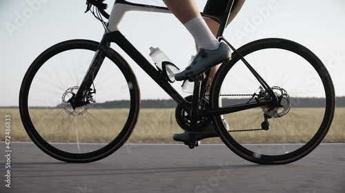Close-up of the legs of a man riding a road bike on a highway at the sunset. Side shot of cyclist riding road bicycle on the background of the field. 50 fps. 4k footage