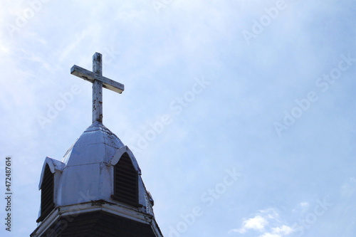 Close-up of a cross at the top of a church steeple. Blue sky with white, wispy clouds as background.