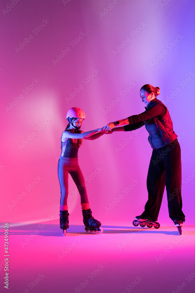 Fototapeta premium child skater athlete holding hands of her trainer, training for competition, photo on pink background in a studio