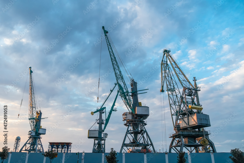 Port cranes close-up against a beautiful blue sky with clouds before sunset. Cargo terminal. Batumi, Georgia