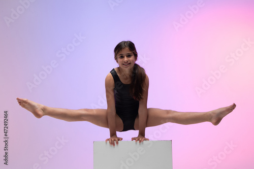 child athlete gymnast performing gymnastic exercise on top of apparatus, training for competition, colored background in a studio