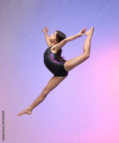 young gymnast athlete performing jumps, training for competition, colorful background in a studio.