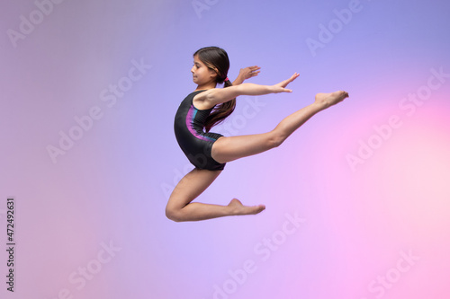 young gymnast athlete performing jumps, training for competition, colorful background in a studio.