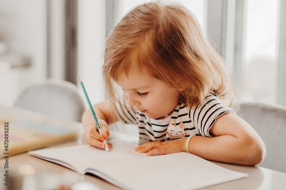 Cute toddler girl sitting in kitchen and drawing while her mother cooking. Cute toddler girl sitting in kitchen and drawing while her mother cooking.