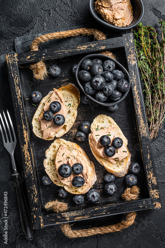 Foie gras toasts, duck liver pate and fresh blueberry in wooden tray. Black background. Top view