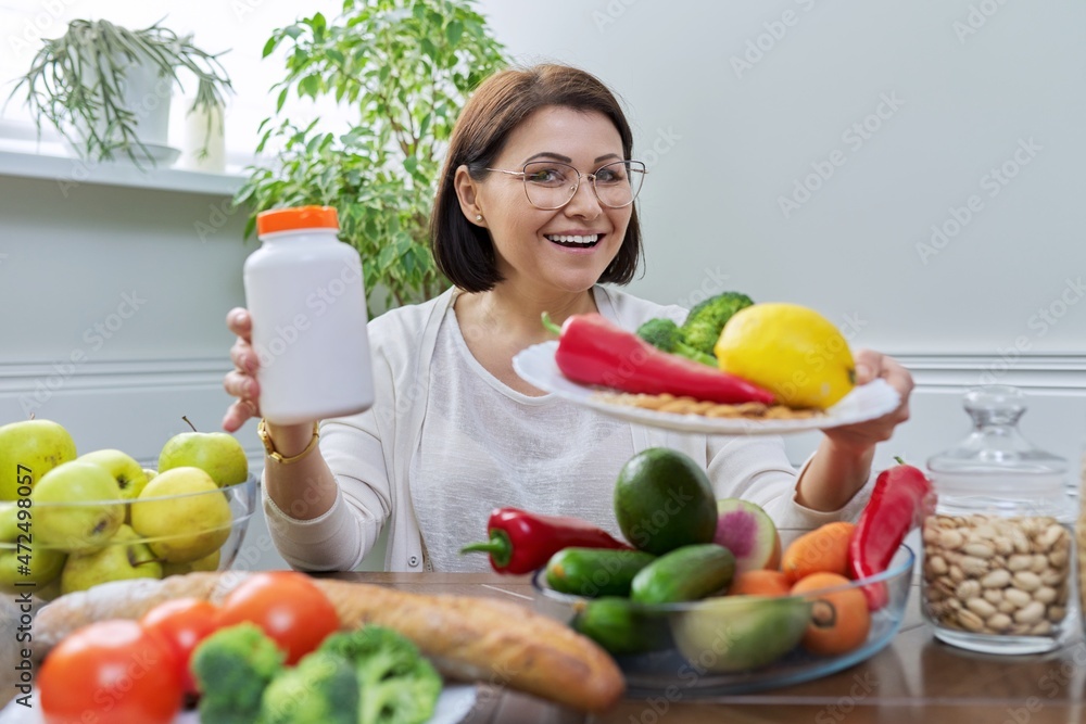 Woman nutritionist pointing at the camera a plate with a set of healthy food and a jar of food additives Woman nutritionist pointing at the camera a plate with a set of healthy food and a jar of food additives
