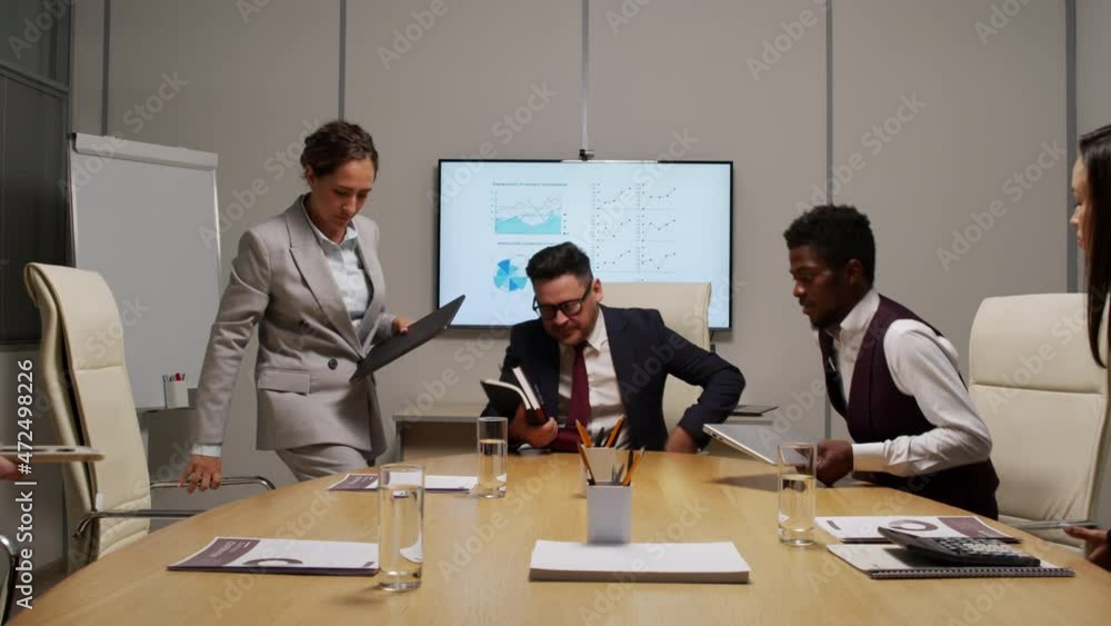 Dolly-out shot of male executive and team of businesspeople sitting down at table in meeting room and getting ready to discussing finances Dolly-out shot of male executive and team of businesspeople sitting down at table in meeting room and getting ready to discussing finances