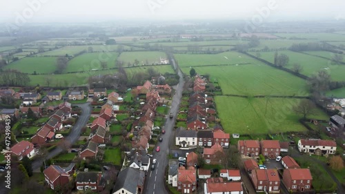 A van / lory driving through a small town in the UK on a misty day. 4K drone footage following a van / lorry. English countryside, in winter. Small town from above. Great Broughton.  photo