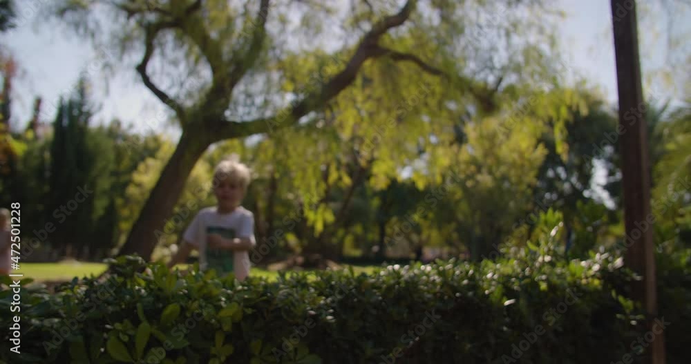 Young european cute blond children walking in a green city park on a sunny summer day, with a white bird feather slowly floating in the foreground Young european cute blond children walking in a green city park on a sunny summer day, with a white bird feather slowly floating in the foreground
