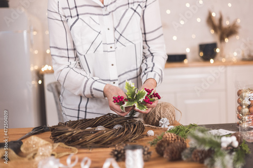 Fototapeta Naklejka Na Ścianę i Meble -  Woman artisan making Christmas holiday wreath on a table among by New Year's decor