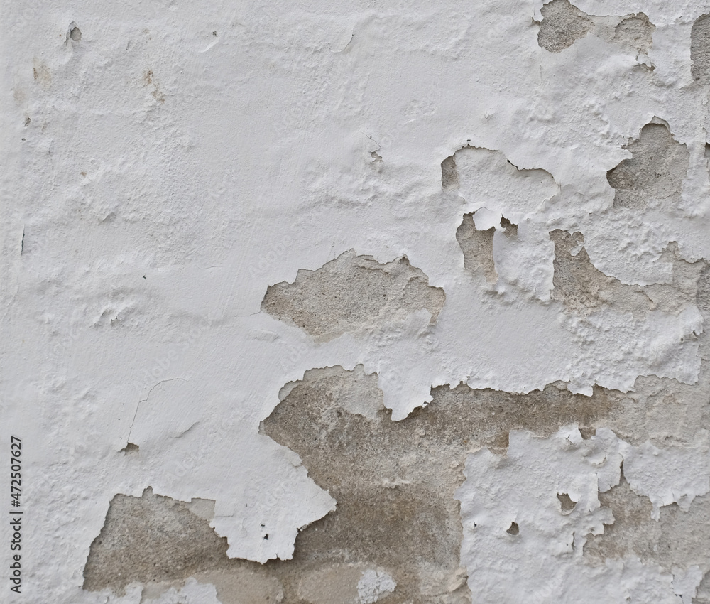 Background of peeling white paint on an old wall. Texture background of an old wall made of gray plaster. Cracks. Copy space. Old peeling plaster wall, crumbles.