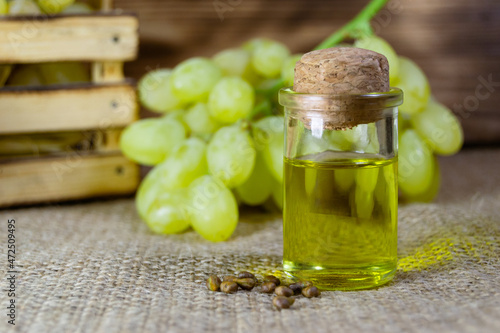 Grape oil seed in small vintage bottle. Heap of grape seeds with green slices and cold press organic essential oil, tincture, extract, infusion on wooden rustic background closeup