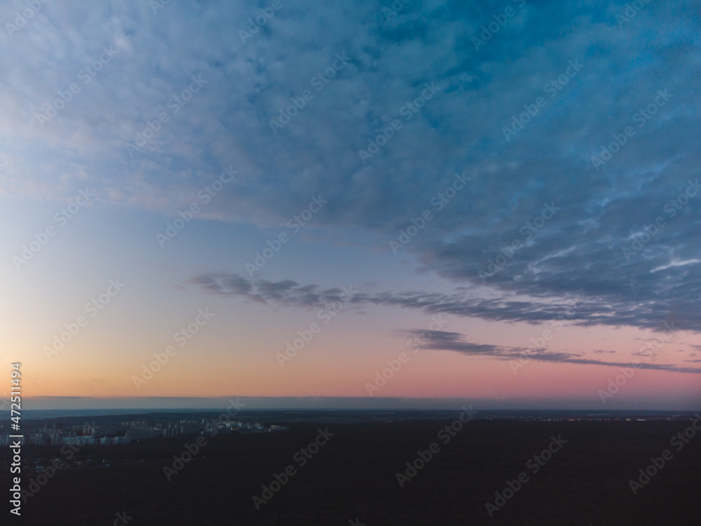Aerial dark cloudscape view above dark forest at sunset. Blue heavy epic clouds covering colorful evening sky scene
