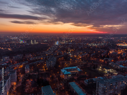 Aerial sunset orange vibrant view on Kharkiv city, Pavlove pole. Night lights on streets of residential district and scenic cloudy sky after sunset. Moody illuminated streets rooftop