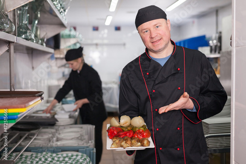 Skilled cook offering to taste just prepared appetizing dish in restaurant kitchen..