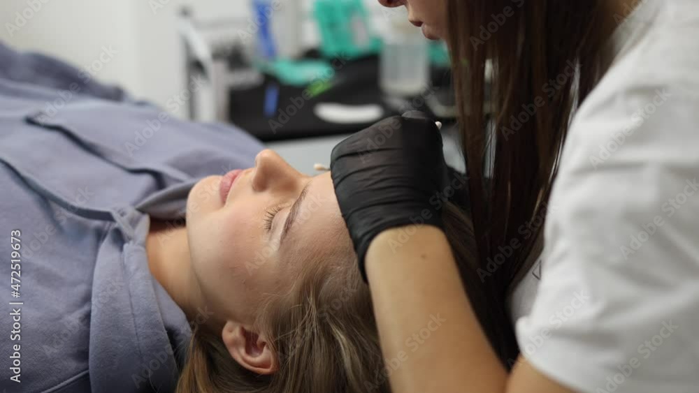 Woman doing eyelashes lamination in beauty studio. Blond hair model has staining, curling, laminating and extension for lashes. Black gloves Woman doing eyelashes lamination in beauty studio. Blond hair model has staining, curling, laminating and extension for lashes. Black gloves