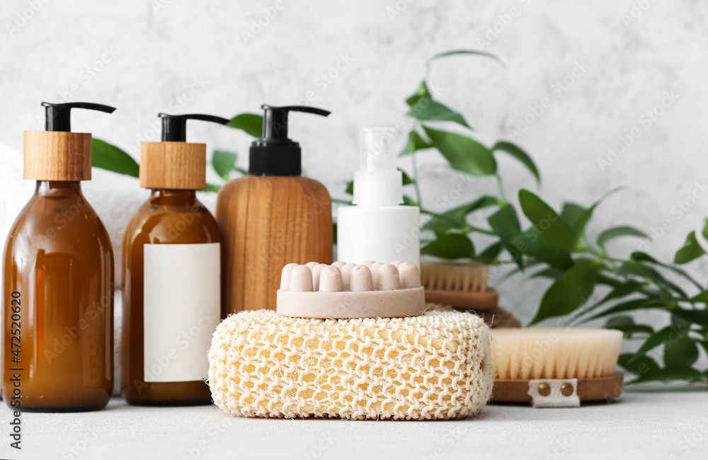 Bath sponge, massage soap bar and bottles of cosmetic products on table against light background Bath sponge, massage soap bar and bottles of cosmetic products on table against light background