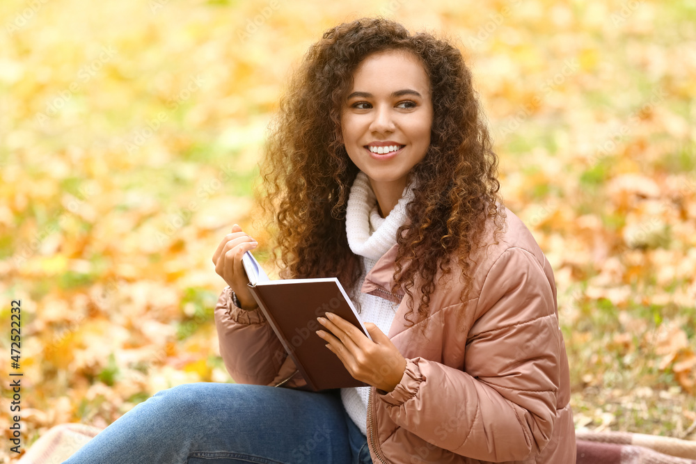 Obraz premium Smiling African-American woman with book in autumn park