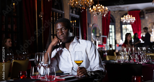Single African-American man with glass of wine sitting in luxury restaurant
