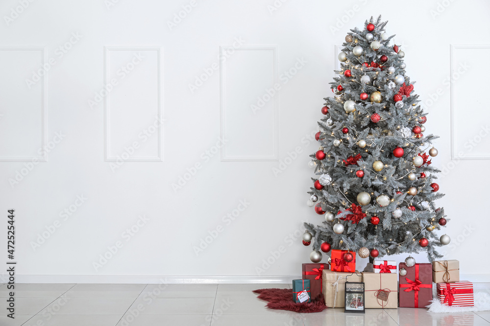 Beautiful Christmas tree and gift boxes near white wall