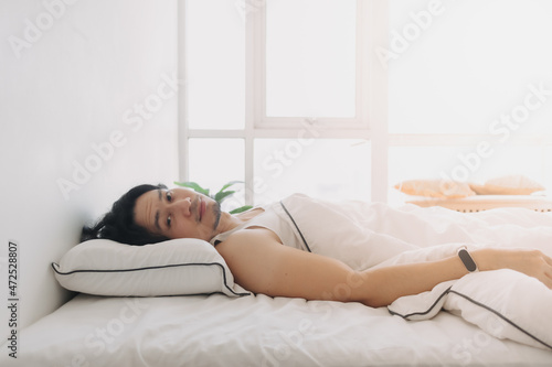 Asian man just wake up in a happy morning in bright white bedroom.