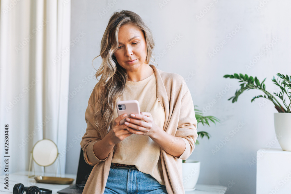 Φωτογραφία Young smiling blonde woman with long hair in stylish cardigan working at laptop